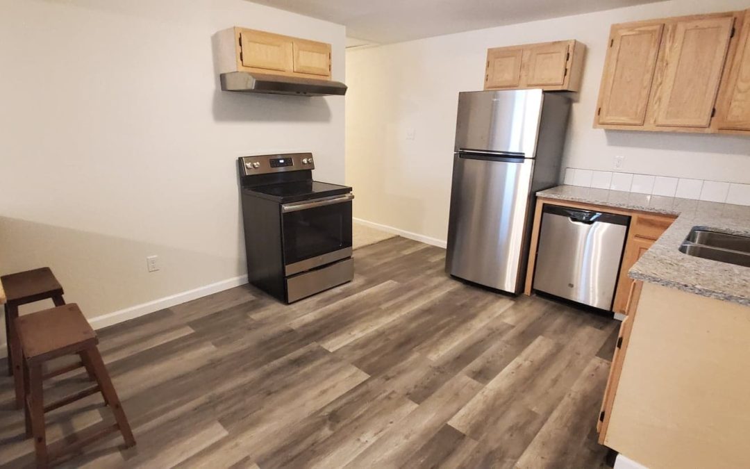Modern kitchen with stainless steel appliances, including a stove, refrigerator, and dishwasher, accented by wooden cabinetry and granite countertops, suitable for apartment living in Little Rock.