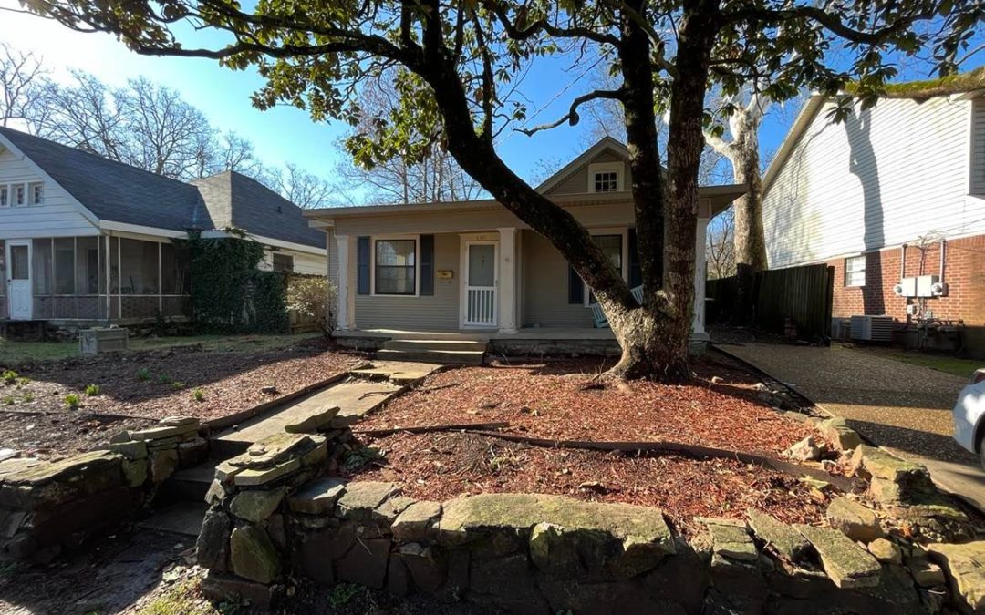 3-bedroom cottage in Historic Hillcrest, featuring a landscaped front yard with a stone border, surrounded by trees and nearby homes, showcasing a charming exterior.