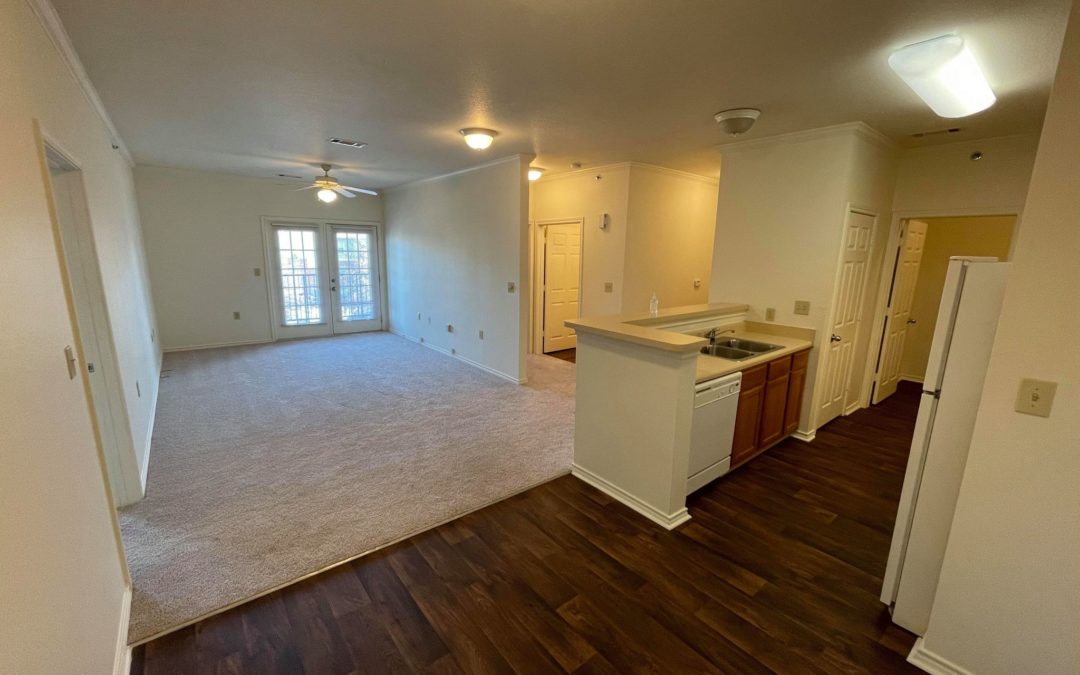 Spacious living area of NLR Hilltop Community apartment featuring open kitchen layout, carpeted flooring, and access to outdoor balcony.