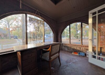 Bright sunroom with large arched windows, wooden desk, and chair, showcasing natural light and a view of the neighborhood, ideal for a cozy living space near UALR.
