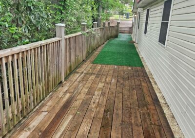 Wooden deck walkway leading to a newly renovated duplex in Midtown Little Rock, featuring green turf and surrounded by lush greenery, highlighting a cozy outdoor space for potential renters.