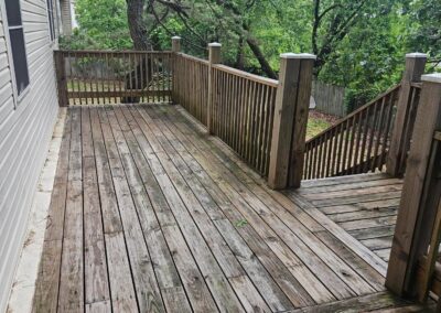 Wooden deck area with railing and stairs, surrounded by lush greenery, showcasing outdoor space of a newly renovated duplex in Midtown Little Rock.