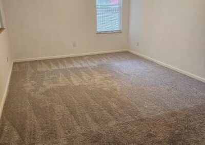 Newly renovated living space with plush carpet, bright window, and neutral walls in Midtown Little Rock duplex.