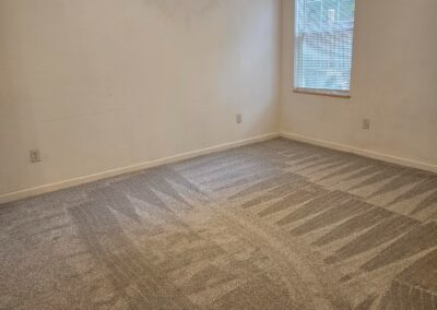 Newly renovated empty room with light gray carpet and large window, showcasing modern updates in a Midtown Little Rock duplex.