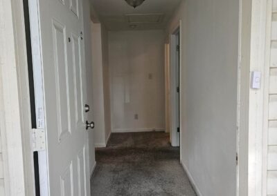 Newly renovated duplex entryway in Midtown Little Rock, featuring a spacious hallway with a front door, light-colored walls, and carpeted flooring, emphasizing modern updates for rental property seekers.