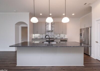 Modern kitchen with large island, pendant lighting, stainless steel appliances, and stylish backsplash in a smart home located in West Little Rock.