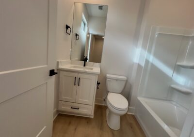 Modern bathroom in brand-new townhome featuring a mirror, sink with cabinet, toilet, and bathtub, showcasing sleek design and hardwood flooring, located in the Argenta District.