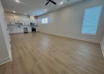 Spacious interior of a brand-new townhome in Argenta featuring champagne-colored hardwood flooring, modern kitchen with stainless steel appliances, and oversized windows.