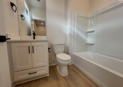 Modern bathroom featuring a white bathtub, toilet, and sleek cabinetry with a mirror, showcasing contemporary design in a brand-new Argenta townhome.