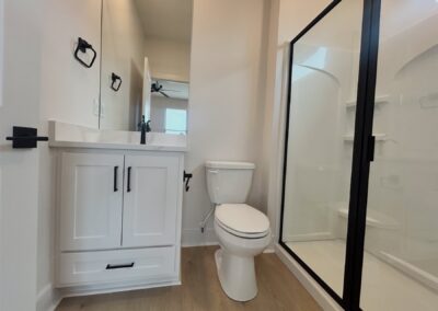 Modern bathroom featuring sleek white cabinetry, a stylish sink, a black-framed shower, and contemporary fixtures, showcasing high-end design elements of the brand-new townhome in the Argenta District.