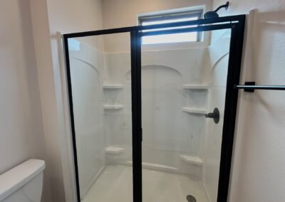 Modern shower enclosure with black frame and clear glass, featuring built-in shelves, in a contemporary bathroom setting.