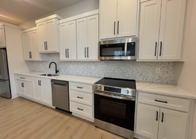 Modern kitchen in brand-new townhome featuring white cabinetry, stainless steel appliances, quartz countertops, and hardwood flooring, located in the Argenta District of Little Rock.