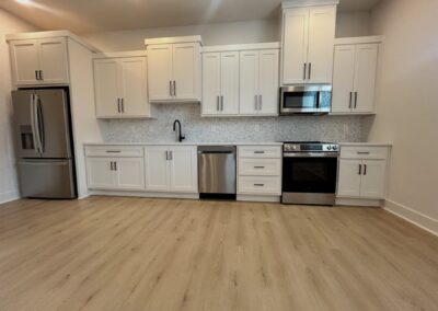 Modern gourmet kitchen in brand-new Argenta townhome featuring white cabinetry, stainless steel appliances, quartz countertops, and champagne-colored hardwood flooring.