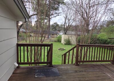 Deck view of fully fenced yard with green grass, trees, and a fire pit, showcasing outdoor space of a fully renovated home in Midtown Little Rock.