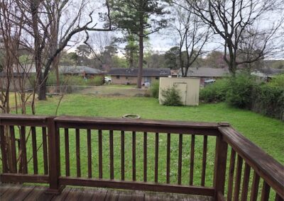View from a wooden deck overlooking a spacious, fenced backyard with green grass, trees, and a storage shed, highlighting the outdoor space of a fully renovated home in Midtown Little Rock.