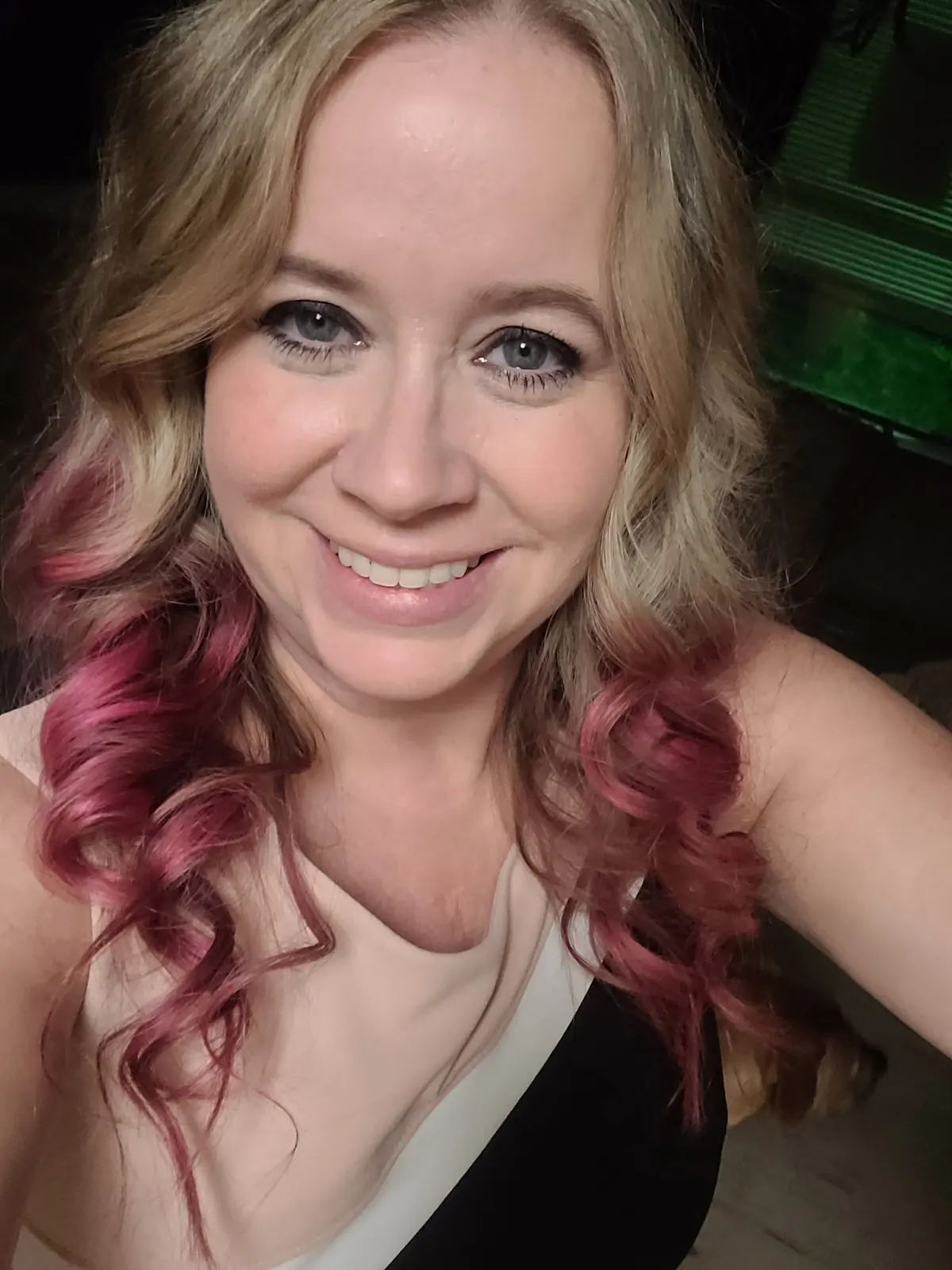 Smiling woman with long, wavy blonde hair featuring pink highlights, wearing a stylish black and beige outfit, showcasing a friendly demeanor, relevant to the Apartment Hunters team introduction.