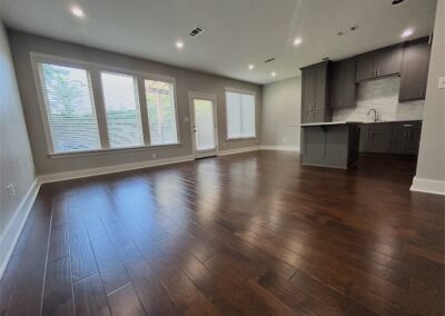 Spacious living area in a modern townhome featuring hardwood flooring, large windows, and a contemporary kitchen with dark cabinetry in Benton, Arkansas.