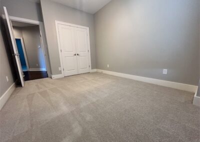 Spacious townhome interior featuring a carpeted room with neutral gray walls, double doors, and a large window, showcasing modern design elements in a Benton, Arkansas rental property.