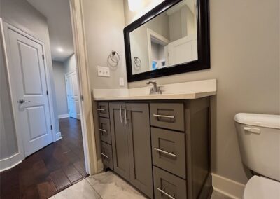 Modern bathroom vanity with gray cabinetry, quartz countertop, large mirror, and white toilet, showcasing spacious design and contemporary finishes in a Benton, Arkansas townhome.