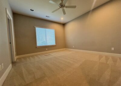Spacious townhome interior in Benton, AR, featuring a well-lit room with a ceiling fan, carpeted flooring, and a window with blinds.
