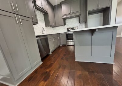 Modern kitchen with gray cabinetry, stainless steel appliances, quartz countertops, and hardwood flooring in a spacious townhome in Benton, Arkansas.