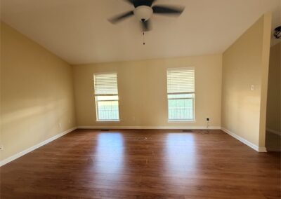 Spacious living room in West Little Rock home featuring hardwood floors, ceiling fan, and natural light from windows.