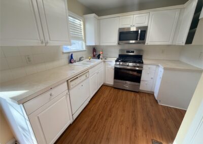 Modern kitchen with white cabinetry, stainless steel appliances including a stove and microwave, and hardwood flooring, showcasing a spacious layout ideal for a two-story home in West Little Rock.