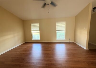Spacious living area in West Little Rock home featuring hardwood floors, two windows with blinds, and ceiling fan, ideal for rental listings.