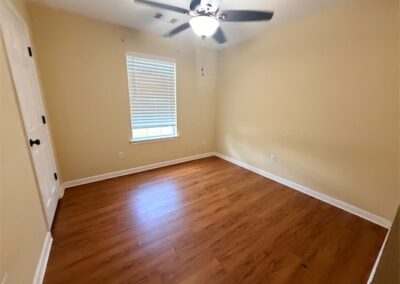 Spacious bedroom in West Little Rock home featuring hardwood floors, ceiling fan, and natural light from window.