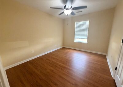 Spacious bedroom with hardwood flooring, ceiling fan, and natural light from window, part of a two-story home in West Little Rock.