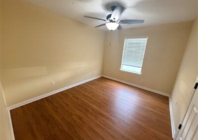 Spacious bedroom in West Little Rock home featuring hardwood floors, ceiling fan, and natural light from window.