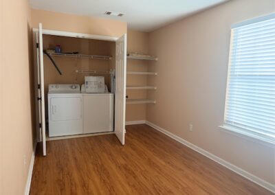 Laundry room with washer and dryer, wooden flooring, shelving, and natural light from window, highlighting spacious design in West Little Rock home.