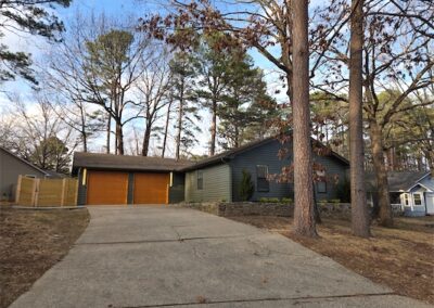 Upgraded 3-bedroom, 2-bath home in West Little Rock with modern exterior, new siding, and two-car garage, surrounded by trees and a private fenced yard.