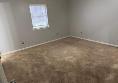 Empty room with beige carpet, light gray walls, and a window with blinds, showcasing spacious layout of single-family home in West Little Rock.